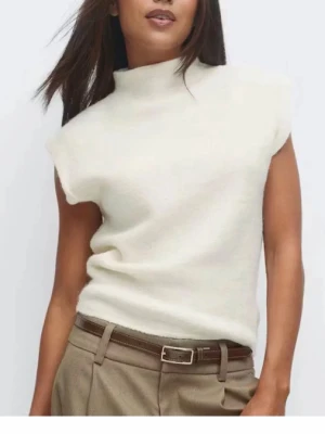 Vit ärmlös topp / T-shirt  polo krage - Säljer en stilren vit polotopp i mjuk ullmix. Toppen är ärmlös med hög krage och har en clean, minimalistisk look som passar perfekt till både jeans och kostymbyxor. Enkel att styla för en trendig och modern outfit.
