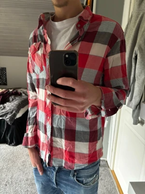 Rutig röd skjorta - Säljer en klassisk rutig skjorta i rött, vitt och svart. Skjortan har långa ärmar, knappar framtill och en avslappnad passform. Perfekt att bära över en t-shirt för en chill look. Tillverkad i mjuk bomull.
