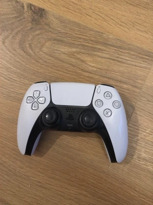 Sony DualSense PS5 handkontroll vit - DualSense handkontroll till PlayStation 5 i vit och svart. Ergonomisk design med två analoga spakar, touchpad, adaptiva triggers och klassiska PlayStation-knappar. Tillverkad i plast och passar perfekt för gaming på PS5.