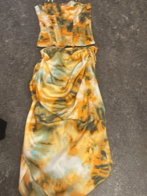 Gult och grönt tie-dye set - Säljer ett snyggt tvådelat set med bustier och kjol i gult, grönt och vitt tie-dye mönster. Bustiern har figurnära passform och kjolen är lång och draperad. Perfekt för dig som vill sticka ut med färg och trendig stil.