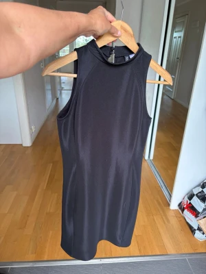 Svart ärmlös kortklänning H&M - Snygg svart ärmlös kortklänning från H&M med hög hals och figurnära passform. Klänningen är enkel och stilren, perfekt för dig som gillar minimalistisk stil. Tillverkad i mjukt och stretchigt material för skön känsla.storlek S. Kan även passa xs och M är stretch 