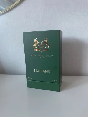 Parfums de Marly Haltane 125ml - Lyxig parfym från Parfums de Marly, modellen Haltane. Flaskan är matt grön med guldfärgat lock och har en elegant relief med två hästar och sköld. Förpackningen är också grön med gulddetaljer och rymmer 125 ml (4.2 fl oz). Perfekt för dig som gillar exklusiva dofter.