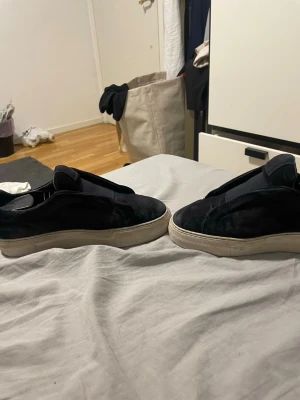 Svarta sneakers från Axel Arigato - Svarta sneakers från Axel Arigato i mocka med chunky vit sula. Slip-on modell utan snörning och med elastiska band på ovansidan för enkel påtagning. Snygg minimalistisk design som passar till det mesta. Slitna från sulan, priset går o diskutera 