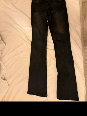 Svarta bootcut jeans med slitningar från bershka - Säljer ett par svarta bootcut jeans med lätt slitna detaljer och klassisk femficksmodell. Jeansen har utsvängda ben och är tillverkade i stretchigt denimtyg för skön passform. Perfekta för en trendig och avslappnad look.