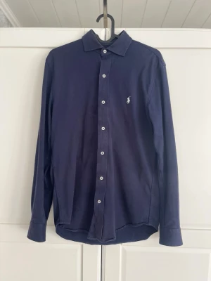 Marinblå skjorta från Ralph Lauren - Säljer nu en riktigt fin Ralph Lauren skjorta i mycket bra skick. Köpte den på Zalando för cirka 2 år sen och har varit sparsamt använd sedan dess. 😃Nypris 1900, mitt pris 700                                                                  Det är storlek S. Bara att höra av sig vid fler frågor eller funderingar. Pris går såklart att diskuteras vid snabb affär. 