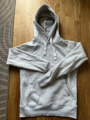 Russemerch hoodie - Snygg ljusgrå hoodie med stor magficka och dragsko i huvan. Klassisk modell med ribbade muddar vid ärmslut och nederkant. Perfekt för chill dagar eller när du vill ha en enkel och clean look.