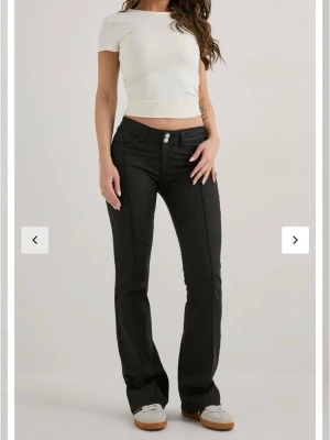 Svarta bootcut jeans med fickor - Snygga svarta bootcut jeans med markerade sömmar och två framfickor. Jeansen är relativt lågmidjade, dubbla knappar och bakfickor med dekorativ söm. Materialet har en lätt glansig finish som ger en cool look. Slutsålda hos Nelly