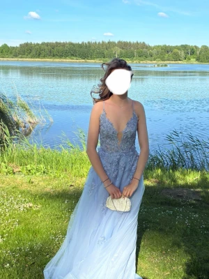 Ljusblå lång/balklänning med spetsdetaljer - Säljer en magisk ljusblå långklänning med tunna axelband och djup v-ringning. Klänningen har vackra spetsdetaljer och broderier på överdelen samt en lång flowy kjol. Perfekt för student eller bal! Använd en kväll!