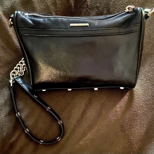 Rebecca Minkoff Mini M.A.C. Läder - Säljer en superfin Rebecca Minkoff Mini M.A.C. Crossbody i svart äkta läder med snygga gulddetaljer. Modellen är en riktig klassiker som passar till allt! Justerbar och avtagbar kedjerem så den kan bäras både som axelremsväska eller som en stilren clutch. Toppskick både utvändigt och invändigt i det svarta fodret. Inga skavanker, se bilder for egen bedömning. Djur- och rökfritt hem. Kan skickas säkert med Plicks frakt! Nypris ca 2200 kr.