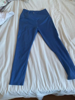 Blå leggings med hög midja - Snygga blå leggings med hög, omlott skuren midja och långa ben. Tillverkade i ett stretchigt material som sitter skönt och har fickor på sidorna. Perfekta för träning eller chill. Passar dig som gillar enkel men trendig stil. V uppe vid midjan som gör dessa perfekta för yoga passet och hur de sitter på en!