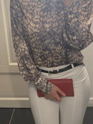 Mönstrad långärmad blus i beige och grå - Säljer en snygg blus med abstrakt mönster i beige och grå toner. Blusen har långa ärmar med knappar vid manschetterna och en avslappnad passform. Perfekt att styla till både jeans och kostymbyxor för en trendig look.