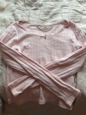Ljusrosa pyjamas tröja 💓 - Söt ljusrosa långärmad topp från H&M med små hålmönster, spetskant vid halsen och en liten rosett framtill. Tillverkad i mjuk bomull, perfekt för en avslappnad och feminin stil. Funkar även som vanlig tröja:)