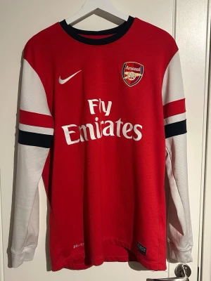 Arsenal långärmad matchtröja Nike - Säljer en autentisk långärmad Arsenal matchtröja från 2012/2013 säsongen. Nike i rött och vitt med svarta detaljer. Tröjan har Arsenal-logga, Fly Emirates-tryck och Dri-FIT-material som andas. Perfekt för fotbollsträning eller att bära på läktaren. Helt okej skick, några små skavanker här och där samt några smutsfläckar - dock inget man tänker på vid användning. Tveka inte att höra av dig vid frågor!