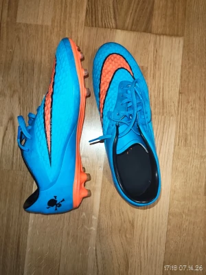Hypervenoms fotbollsskor - Säljer ett par snygga fotbollsskor i blått med orangea detaljer och dobbar. Skorna har snörning, låg profil och ett coolt dödskalletryck på hälen. Perfekta för konstgräs eller gräsplan. Materialet är syntet för bra grepp och känsla på planen.