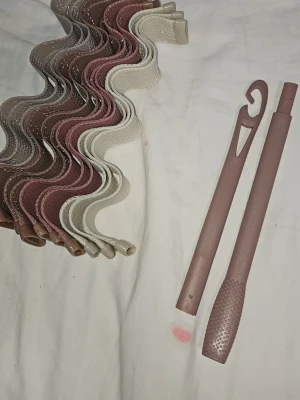 Vågiga hårspolar i rosa och beige - Säljer ett set med vågiga hårspolar i meshmaterial i färgerna beige, rosa och brunt. Medföljer gör även en rosa plastkrok för enkel applicering av spolarna i håret. Perfekt för att skapa mjuka lockar utan värme.