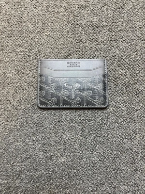 Svart kortfodral från Goyard - Snyggt svart kortfodral från Goyard med klassiskt mönster i vitt och grått. Fodralet har flera kortfack på både fram- och baksidan och är gjort i läder med canvasdetaljer. Perfekt för dig som vill ha en stilren och exklusiv accessoar.