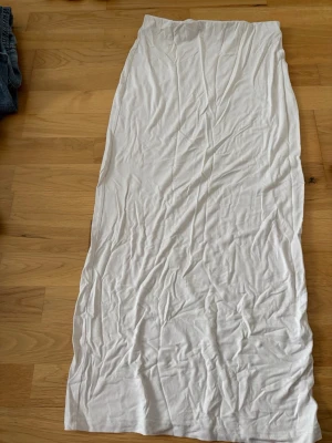 Vit långkjol i mjukt material - Säljer en enkel och stilren vit långkjol i mjukt och stretchigt material. Kjolen har rak passform och är perfekt för varma dagar. Passar till både sneakers och sandaler.