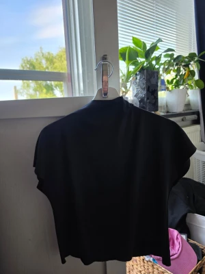 Svart croppad polotopp - Snygg svart croppad polotopp med korta ärmar och tight passform. Perfekt till jeans eller kjol för en trendig look. Enkel och stilren design utan mönster eller detaljer.