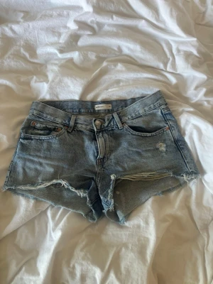 Ljusa denimshorts med slitningar - Säljer ett par ljusblå denimshorts med slitna detaljer framtill. Klassisk femficksmodell med knapp och dragkedja. Köpta förra året, använt fåtal gånger. Säljer då de är en aning försmå för mig.💕