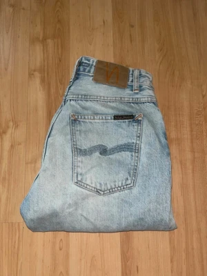 Nudie jeans  - Snygga ljusblåa jeans från nudie jeans. Midja 33cm, längd 98cm. JAG SKICKAR EJ FLER BILDER NÄR JAG BÄR JEANSEN! för bättre inblick i passformen rekommenderar jag att googla på modellnamnet. För storleksguide kolla måtten noggrant då jeansen alltid kan vara uppsydda heller krympta och jag ej tar emot returer :) s6,3