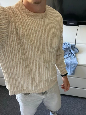 Beige stickad tröja från ZARA - Säljer en snygg beige stickad tröja från ZARA i storlek M. Tröjan har ett ribbat mönster, rund halsringning och är gjord i mjukt material. Perfekt för dig som gillar en stilren och avslappnad look.