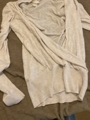 Ljusbeige tunn kofta - Säljer en ljusbeige, tunn och mjuk kofta med öppen front och långa ärmar. Perfekt att slänga över en t-shirt eller linne för en avslappnad look. Materialet känns lätt och luftigt, vilket gör den skön att bära inomhus eller under en jacka.