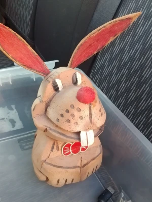 Träkanin med röda öron och fluga - Säljer en handgjord kaninfigur i trä med stora röda öron, röd nos och en röd fluga. Kaninen har målade detaljer som vita tänder och svarta ögon. Perfekt som dekoration till påsk eller som rolig inredningsdetalj.