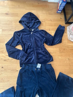 Mörkblå velour loungewear-set - Mysigt loungewear-set i mörkblå velour med hoodie och dragkedja samt matchande byxor med resår i midjan. Perfekt för chill dagar hemma. Materialet är mjukt och stretchigt för extra komfort.