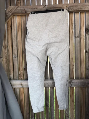 Gråa mjukisbyxor med resårmidja - Ett par klassiska grå mjukisbyxor i mjukt bomullsmaterial. Byxorna har resår i midjan och smalare benavslut för en skön och avslappnad look. Perfekta för chill dagar hemma eller när du vill vara bekväm. Enkla att matcha med hoodie eller t-shirt.