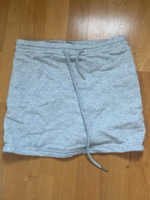 Grå kortkjol med snörning - Snygg ljusgrå kortkjol med snörning i midjan. Kjolen är i mjukt material och har en vit innershorts.