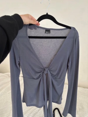 Blå  långärmad topp med knyt - Snygg långärmad topp med djup v-ringning och knyt framtill. Tillverkad i ett mjukt och stretchigt material som sitter bekvämt på kroppen. Perfekt att styla med jeans eller kjol för en trendig look.