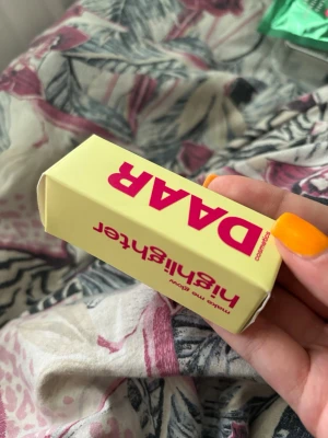 DAAR highlighter stick - Highlighter i stickformat från DAAR med ljus, champagnefärgad ton. Kommer i en söt, ljusgul förpackning med rosa text. Enkel att applicera direkt på huden för en naturlig glow. Perfekt att ha i väskan för touch-ups när som helst. ALDRIG ANVÄND BARA ÖPPNAD