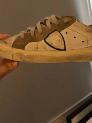 Vita och grå sneakers från Philippe Model - Snygga sneakers från Philippe Model i vitt och grått med klassisk låg siluett. Skorna har mockadetaljer, vita skosnören och den ikoniska logotypen på sidan. Perfekta för en avslappnad streetstyle-look.dom är väl använda men funkar bra