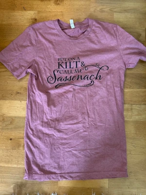 Rosa T-shirt Outlander - ’Put on a kilt and call me Sassenach’. Outlander. Need I say more? Inköpt ifrån Etsy. Använd en till två gånger. Fint skick. Storlek S / 36. 