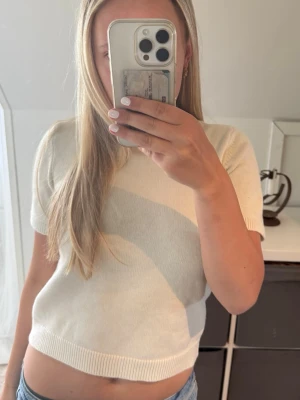 Vit stickad kortärmad tröja - Säljer en stilren vit stickad tröja med korta ärmar och rund hals. Tröjan har en rak passform och ribbstickade detaljer vid ärmslut, halsringning och nederkant. Perfekt till jeans eller kjol för en enkel och fräsch look.