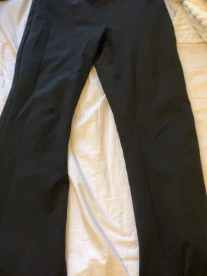 Svarta raka kostymbyxor - Säljer ett par klassiska svarta kostymbyxor med bootcut passform. Byxorna har enkel design utan synliga detaljer och är tillverkade i ett slätt tyg som ger en stilren look. Perfekta för dig som gillar minimalistisk stil.