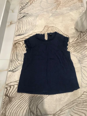 Mörkblå spetsblus med korta ärmar - Snygg mörkblå blus med kortärmade spetsdetaljer och rund hals. Materialet är lätt och luftigt, perfekt för att skapa en stilren look. Spetsen på ärmarna ger en extra touch av elegans. Använd endast ett fåtal gånger. Är öppen med prisförslag😊