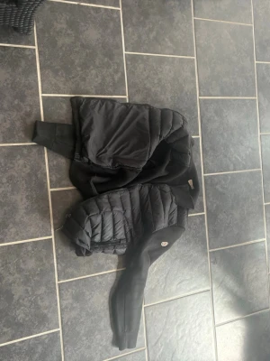 Svart pufferjacka från Moncler - Säljer en svart pufferjacka från Moncler med quiltade partier och mjuka ärmar. Jackan har dragkedja framtill och Moncler-logga på ena ärmen. Perfekt för kalla vinterdagar och riktigt snygg till streetwear-stilen.