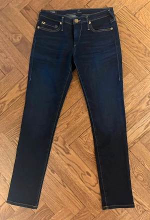 Mörkblå skinny jeans från True Religion  - (Pris kan diskuteras) Säljer ett par mörkblå super skinny jeans från True Religion med klassisk femficksmodell och guldfärgade detaljer. Jeansen har medelhög midja och stretchigt material som sitter tight hela vägen ner. Perfekta för dig som gillar en slimmad siluett. Den har en liten fläck på baksidan men ganska säker på att det går bort i tvätten. ❤️❤️storlek 27 