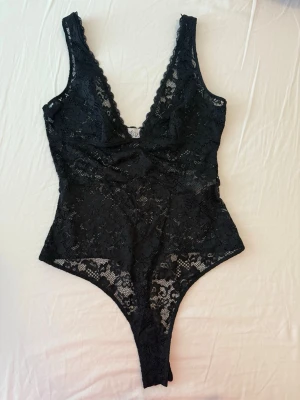 Bodysuit in black från OhPolly - Sheer Lace Scalloped Plunge-Neck Bodysuit in Black  från OhPolly. Om du undrar hur den ser ut på sök på deras hemsida ”Zayla” så får du upp bilden. Storlek Eu 36 alltså storlek S. Använt en gång. Ordinarie pris: 445kr på hemsidan. Pris går att diskutera. Made from premium lace fabric with a mesh lining. Partially lined.   This style is intentionally sheer.  Shell: 90% Polyamide, 10% Elastane; Lining: 92% Polyester, 8% Elastane. Man kan använda nipple covers. Går att styla med kostymbyxor.