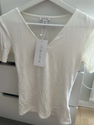 Vit v-ringad t-shirt från Newyorker - Säljer en enkel och stilren vit t-shirt från Amisu (Newyorker) med v-ringning och korta ärmar. T-shirten är gjord i mjuk bomull och har en normal passform som sitter snyggt på kroppen. Perfekt basplagg till garderoben. Sitter som S. Lappen är kvar