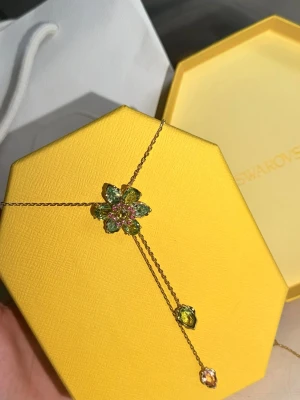 Blommigt halsband från Swarovski - Vintage  halsband från Swarovski med en blomformad hängare i gröna och rosa kristaller. Kedjan är i guldfärg och har två droppformade hängen i gult och klart glas. Blomman är justerbar och den är oanvänd det enda gången den användes va när jag tog ner bilderna. Perfekt för dig som gillar färgglada och eleganta accessoarer. Kommer även med lådan och påsen 