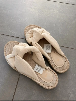 Beige sandaler med knut från H&M - Säljer ett par snygga beige sandaler från H&M med breda tygband och stor knut framtill.💗