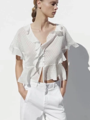Vit volangblus med prickigt mönster från Zara - Söt och luftig vit blus med volanger och diskret prickigt mönster. Blusen har korta ärmar, knappar framtill och är tillverkad i ett tunt, transparent material som ger en romantisk vibe. Perfekt för dig som gillar trendiga och söta plagg.