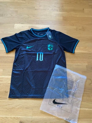 Svart Brasilien Neymar Jr Nike Concept kit 2026 - Snygg svart Brasilien fotbollströja från Nike med Neymar Jr och nummer 10 på ryggen. Tröjan har turkosa detaljer, korta ärmar och är tillverkad i ett lätt, andningsbart material perfekt för träning eller match.