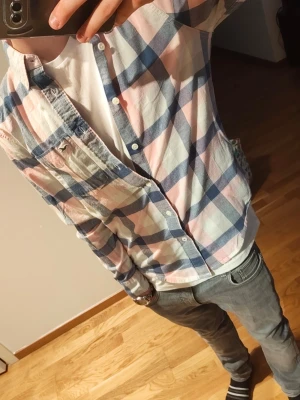 skjorta från Hollister XS - Säljer en rutig skjorta från Hollister i ljusblå, rosa och vit. Skjortan är i stretchigt bomullsmaterial och har knappar framtill samt en bröstficka. Perfekt för en avslappnad och snygg stil.