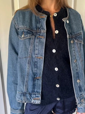 Ny Klassisk blå jeansjacka jeans jacka Gina Tricot  - Säljer en klassisk blå jeansjacka i rak modell med knappstängning framtill och två bröstfickor med lock. Jackan har silverfärgade knappar och tydliga sömmar som ger en tidlös look. Perfekt att slänga över en t-shirt eller hoodie för en avslappnad stil. Utan krage 