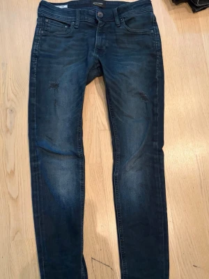 Mörkblå skinny jeans från Jack & Jones - Snygga mörkblå skinny jeans från Jack & Jones med lätt slitna detaljer på framsidan. Klassisk femficksdesign och stretchigt material som ger en bekväm passform. Perfekt för dig som gillar en modern och slim look. Storlek 28/30