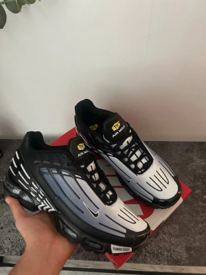 Nike Air Max Plus 3 svart/vit - Nike Air Max Plus 3 sneakers i svart och vitt med gradient-effekt på ovandelen. Skorna har synliga Air Max-enheter i sulan, svarta snören och detaljer i gult på plösen. Ovandelen är i mesh och syntetmaterial med Tuned Air-dämpning för extra komfort.