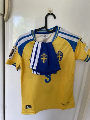 Svensk landslagströja Adidas gul/blå - Säljer en gul och blå svensk landslagströja från Adidas med nummer 9 på framsidan och officiella landslagsmärken. Tröjan har korta ärmar, blå detaljer och Aeroready-material för bra ventilation. Perfekt för fotbollsfans och matcher.